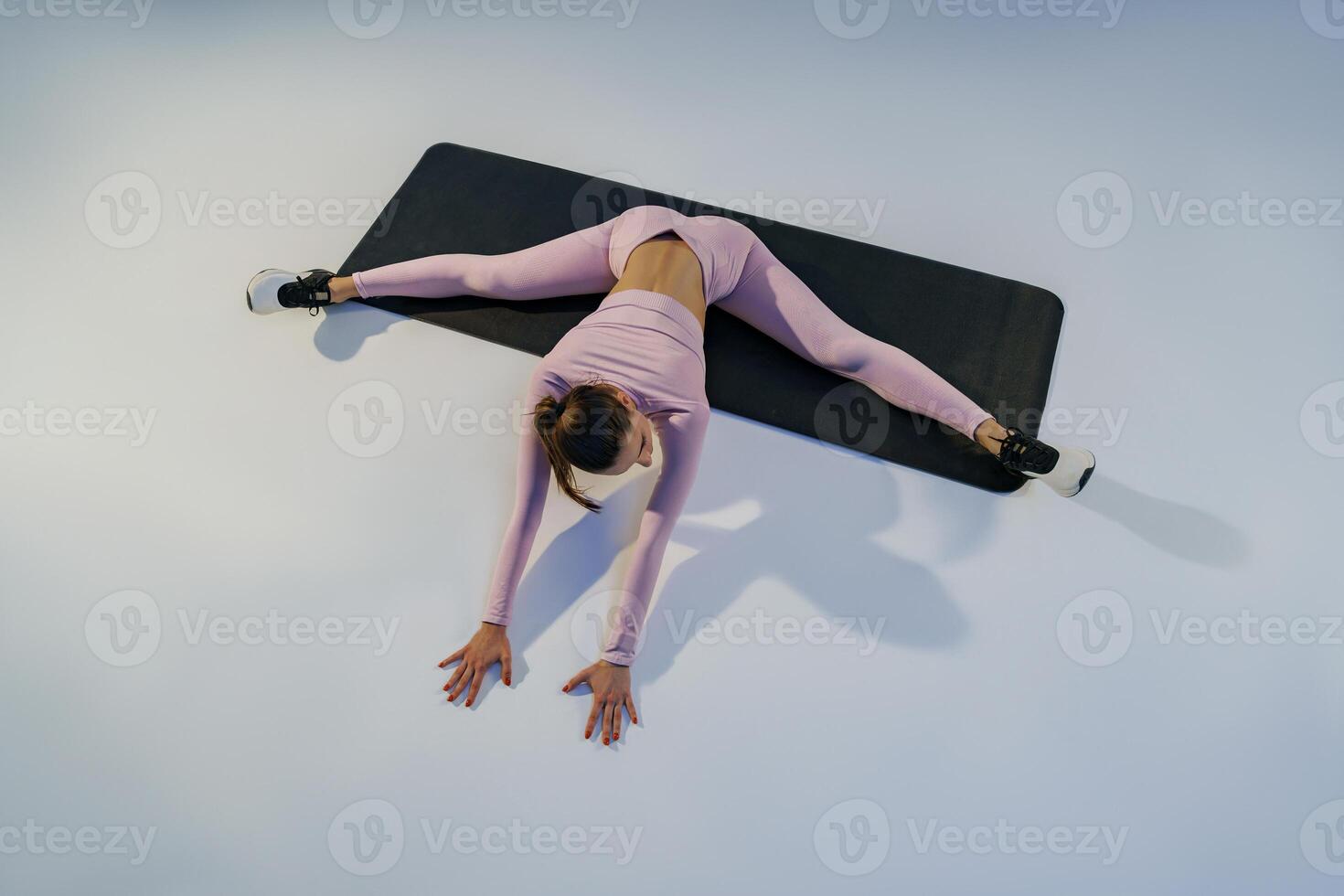 Flexible woman doing stretching exercises on yoga mat on studio background. Healthy lifestyle photo