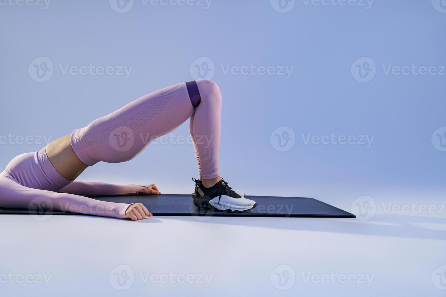 Close up of woman lying on yoga mat and trains legs with fitness elastic band on studio background photo