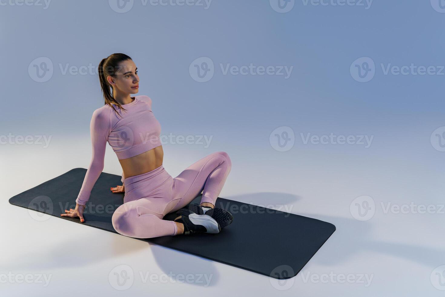 Woman wearing sportswear doing stretching exercises on yoga mat on studio background photo
