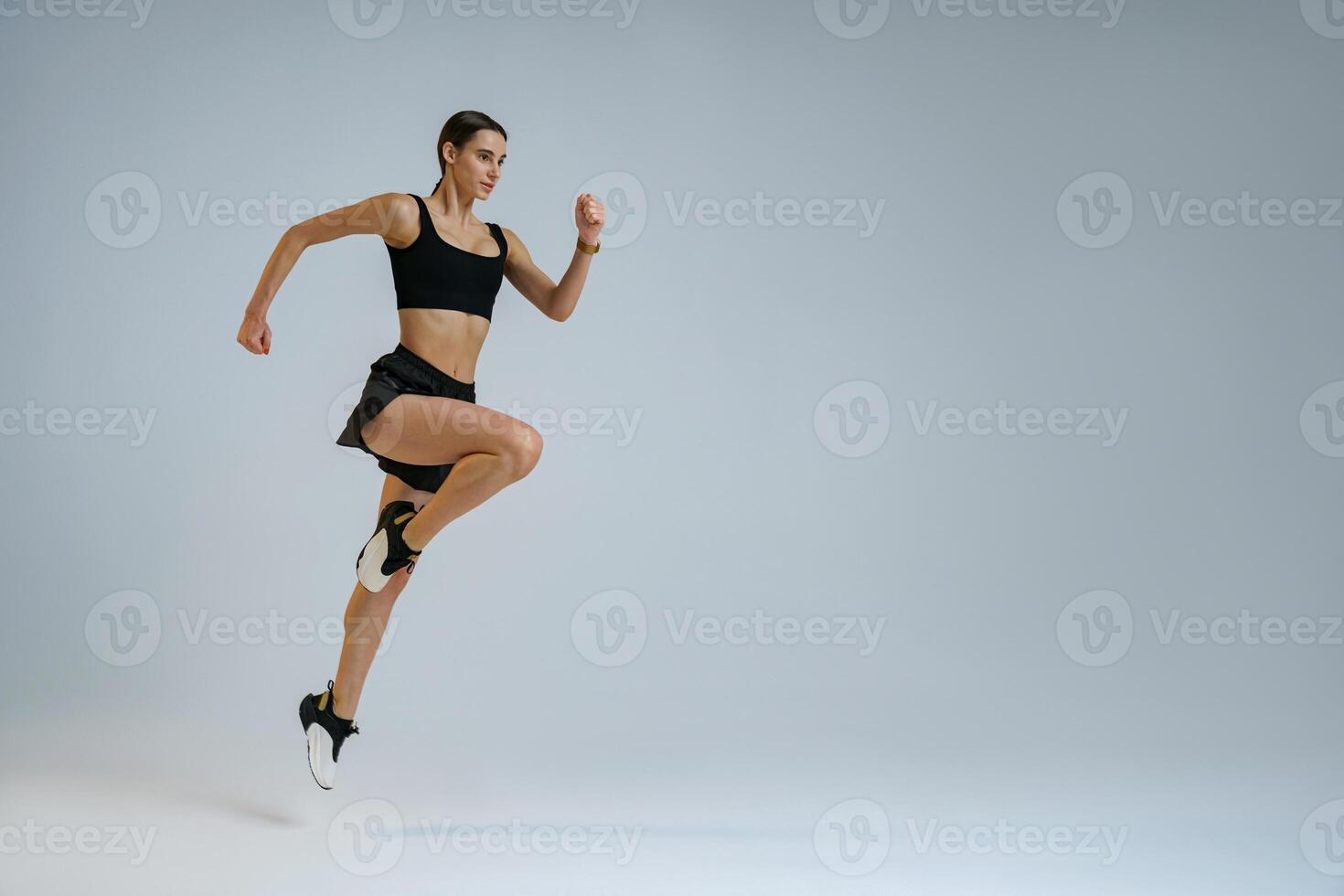 Determined sporty woman running in Mid-Air exercising during cardio workout over studio background photo