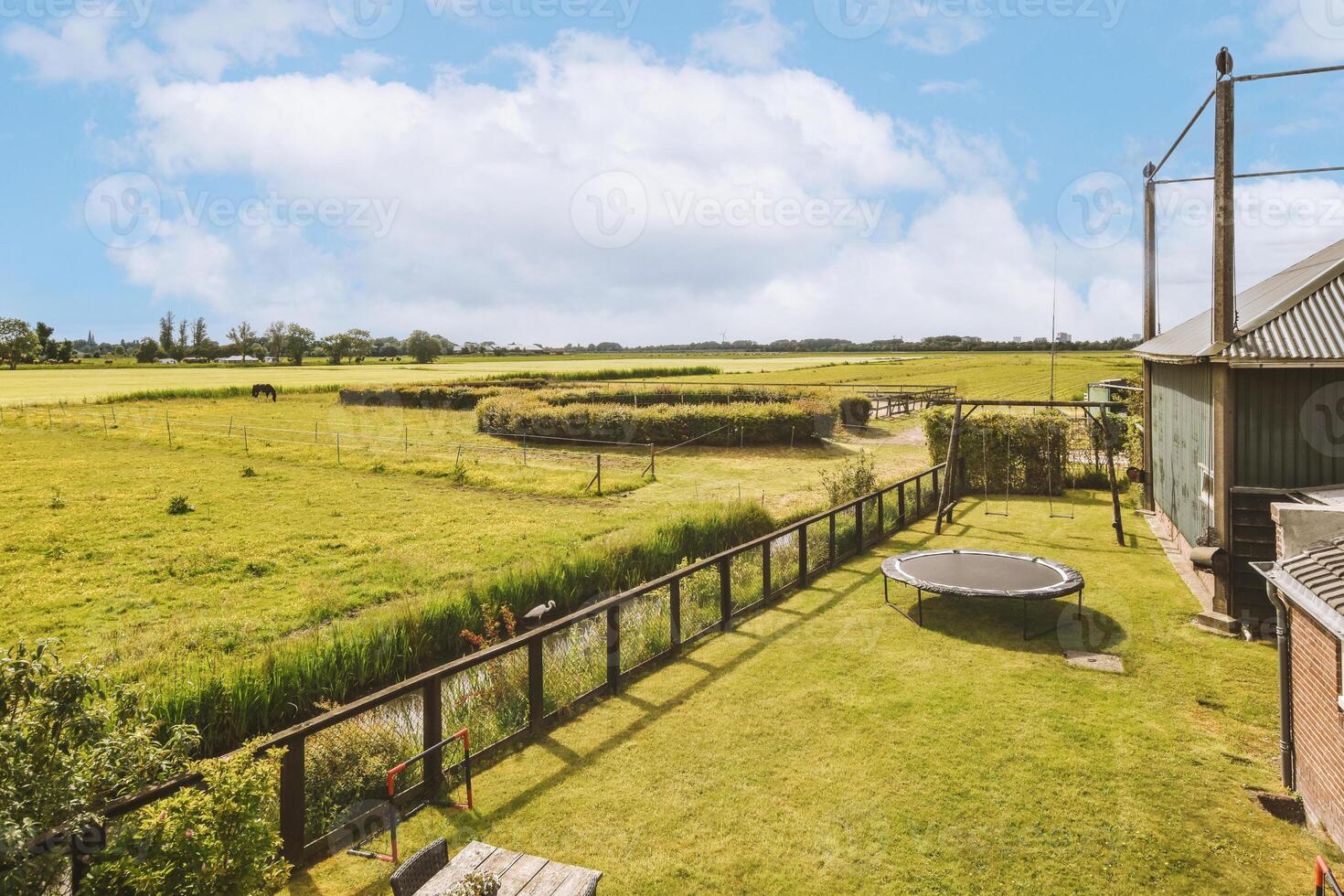A view of a green field with a barn and a trampoline photo