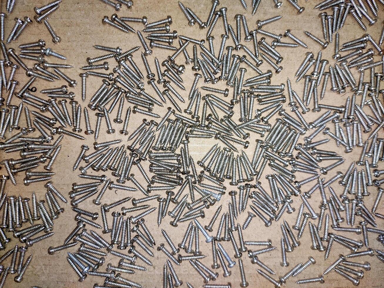 A high-resolution image of a pile of identical screws, showcasing their consistent size and shape. The screws are arranged in a unsorted pattern on a brown background. photo