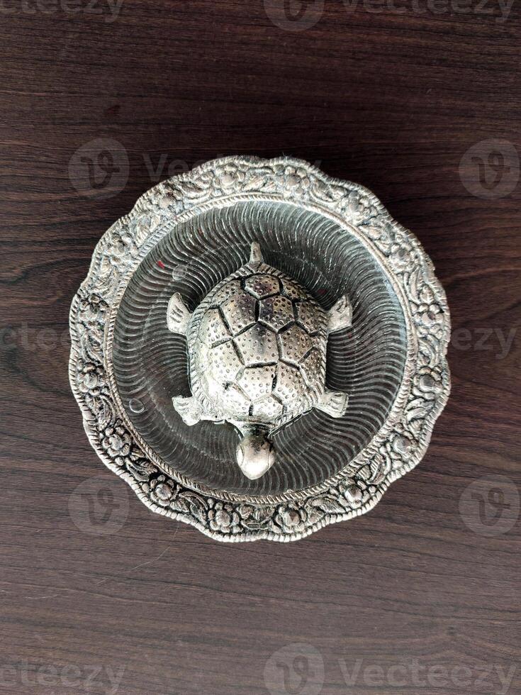 A top-angle view of a silver-plated tortoise figurine resting on a wooden surface, showcasing its intricate design and reflective finish against the rich wood grain. photo