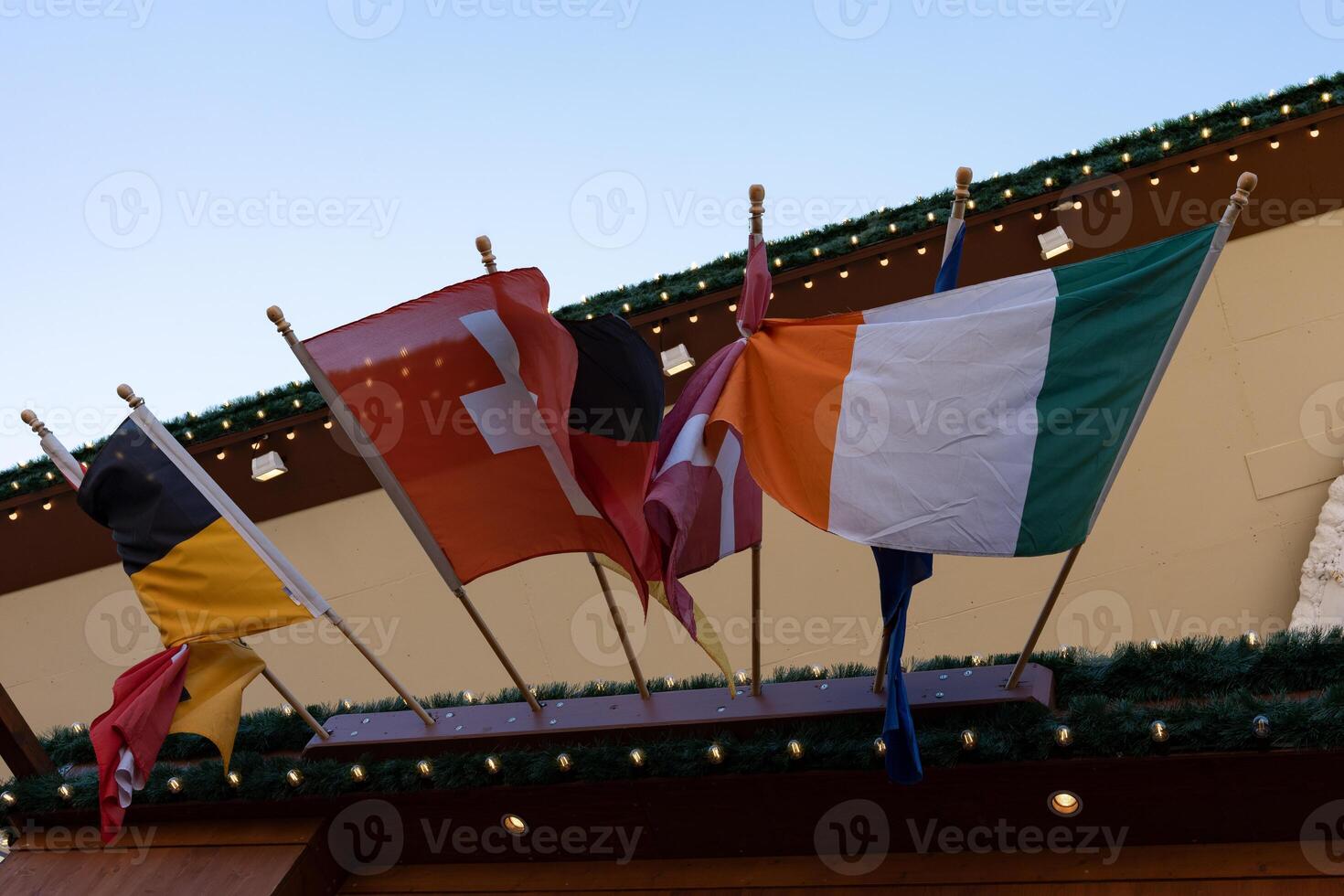 Several flags of different countries intertwine together in the wind. Flag of Ireland, flag of Switzerland, flag of Germany. photo