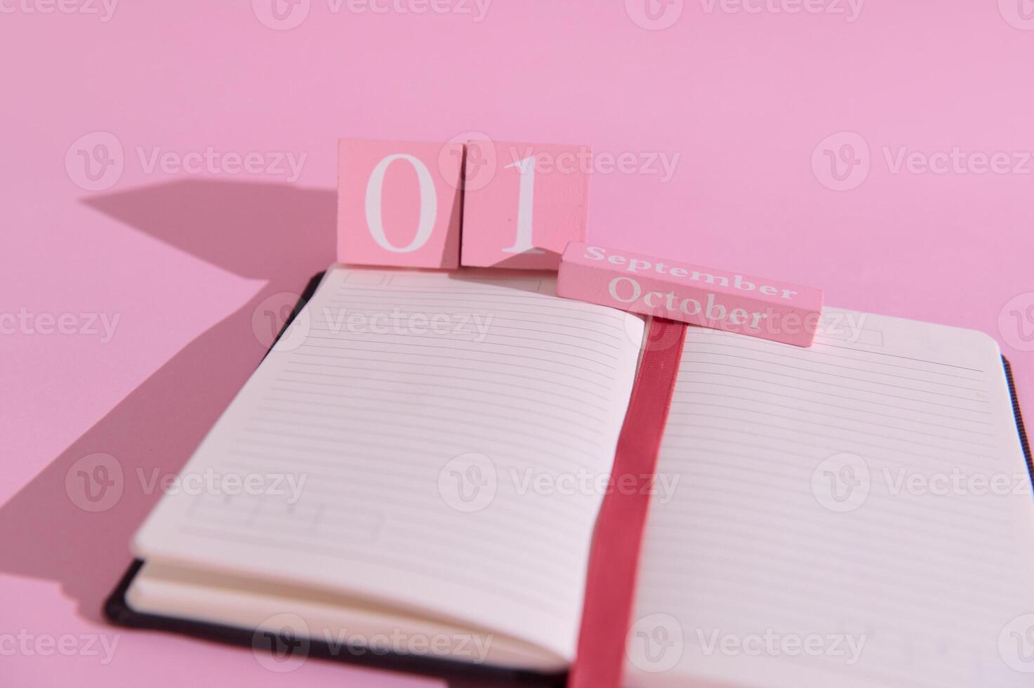 Open notebook with pink calendar blocks marking October 1st on a vibrant pink background, symbolizing planning and organization. photo