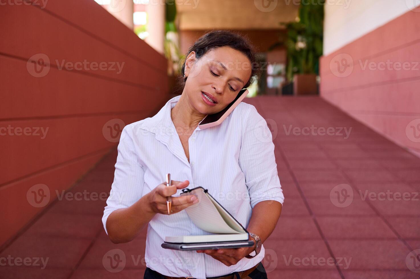 Businesswoman multitasking with a phone call and scheduling notes in a modern office corridor photo