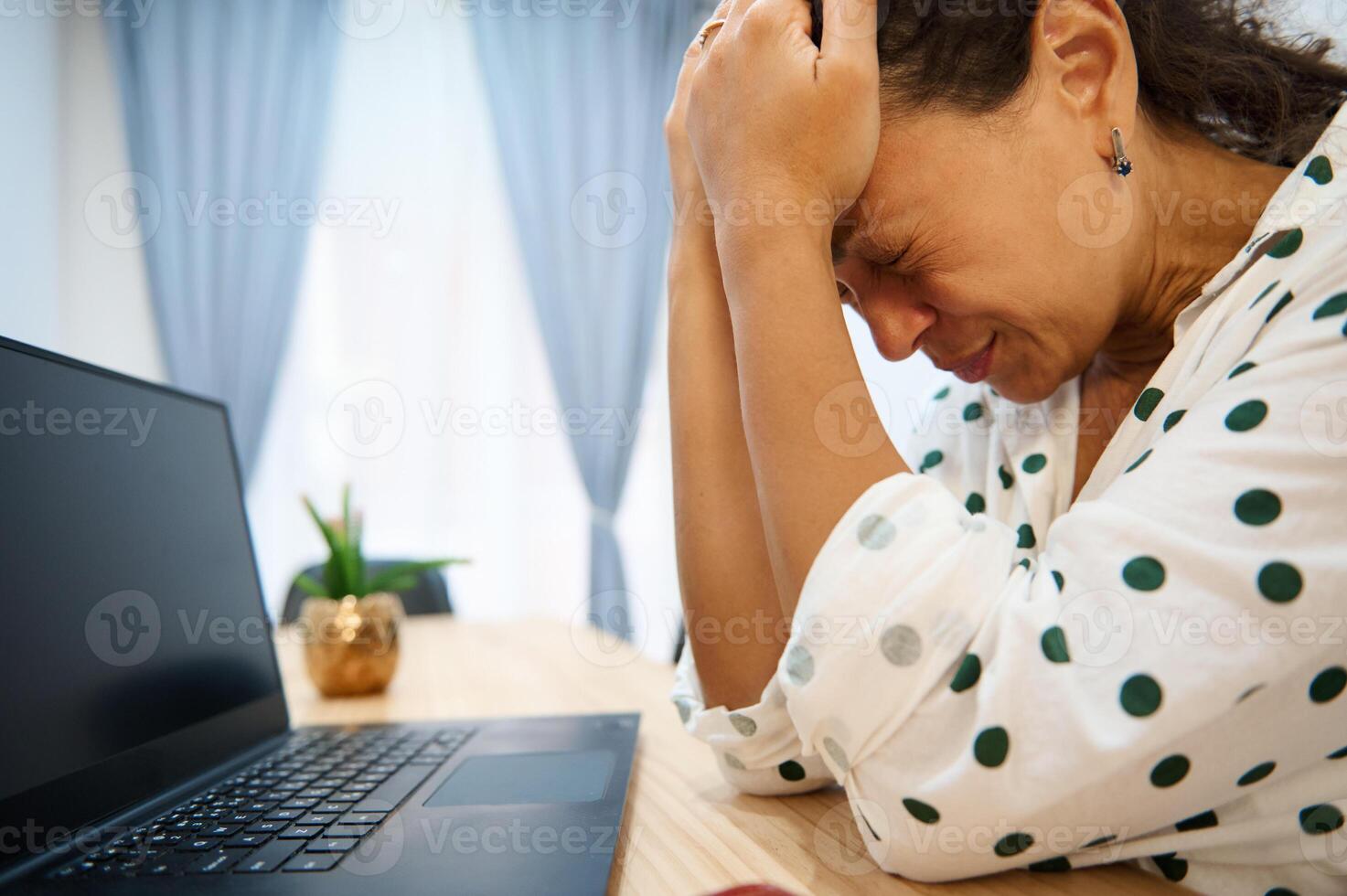 Stressed woman sitting at desk with hands on head next to laptop. Experiencing work frustration or burnout in modern office setting. photo