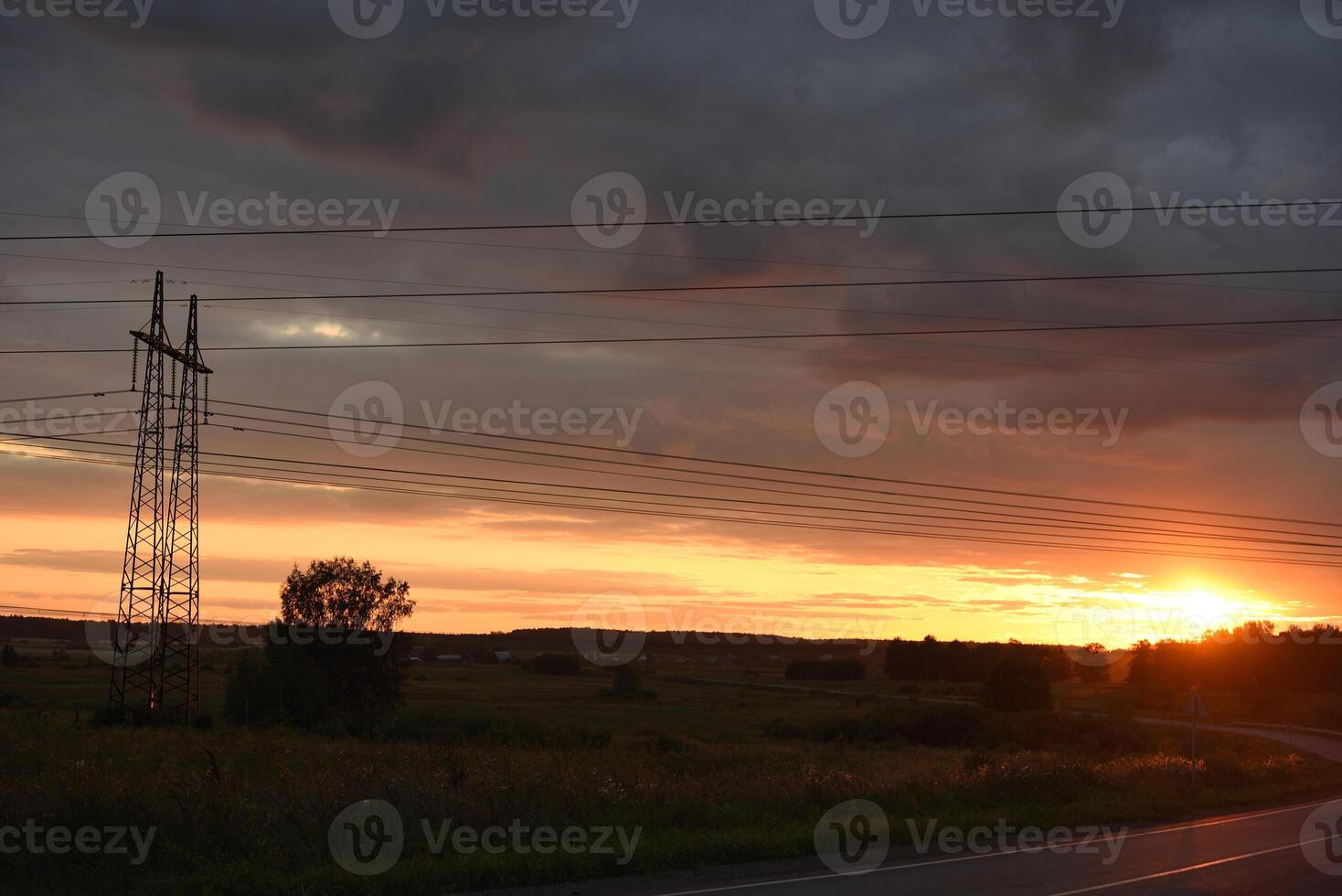 The evening landscape and the setting sun. High-voltage wires and an asphalt road in the evening. photo