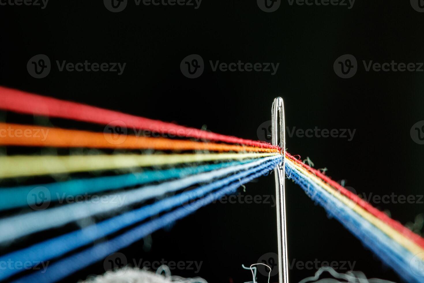 multi-colored threads for sewing in the form of a rainbow pass through an antique needle on a black background photo