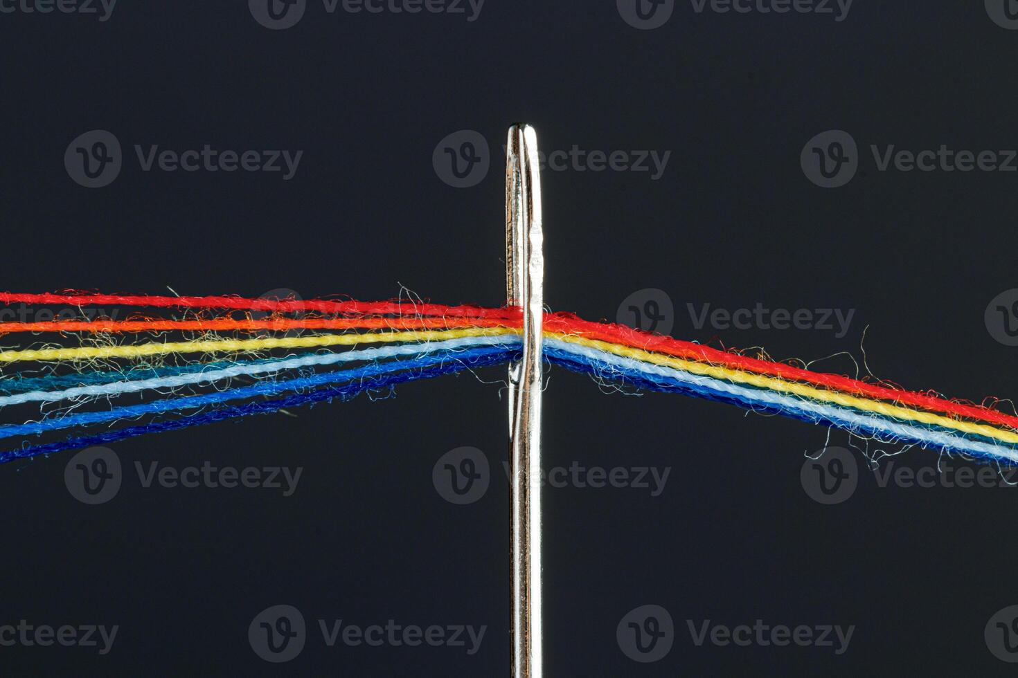 multi-colored threads for sewing in the form of a rainbow pass through an antique needle on a black background photo