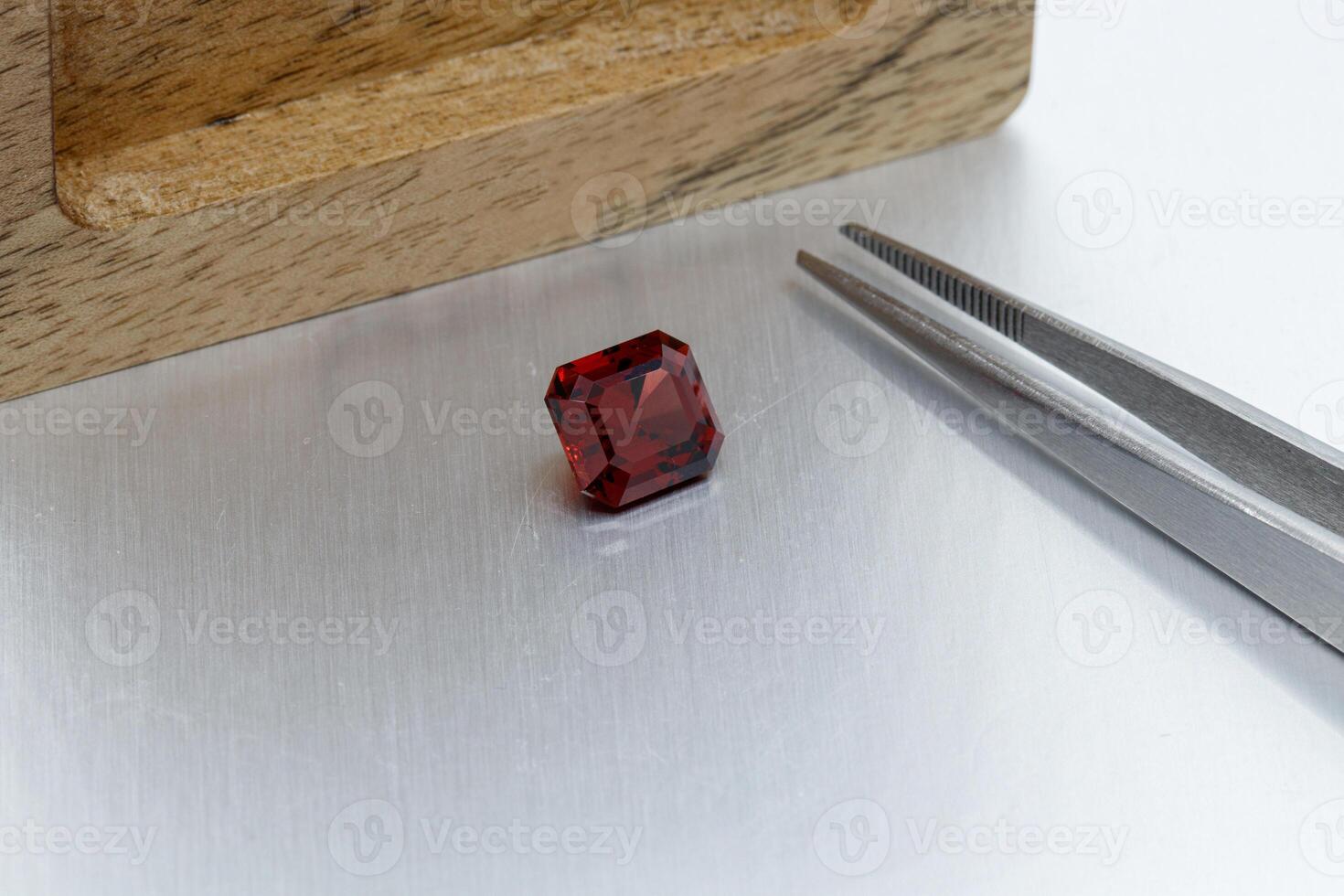 macro mineral faceted stone Garnet with tweezers on a gray background photo