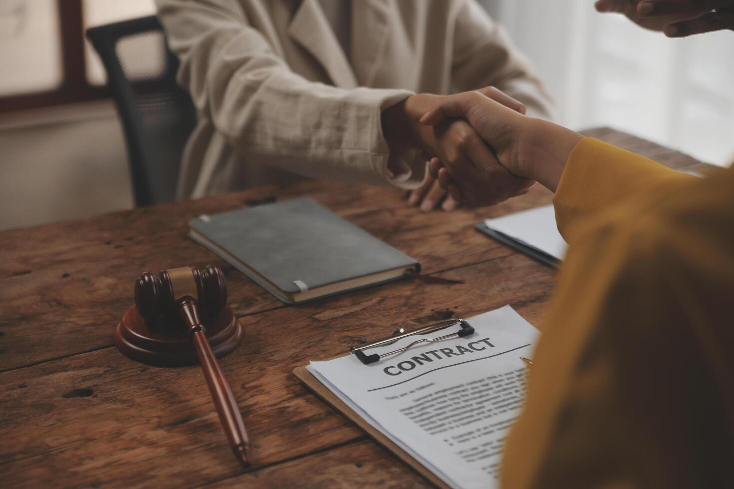 Lawyer shaking hands with a client making about documents, contracts, agreements, cooperation agreements with a female client at the lawyer's desk and a hammer at the table. photo