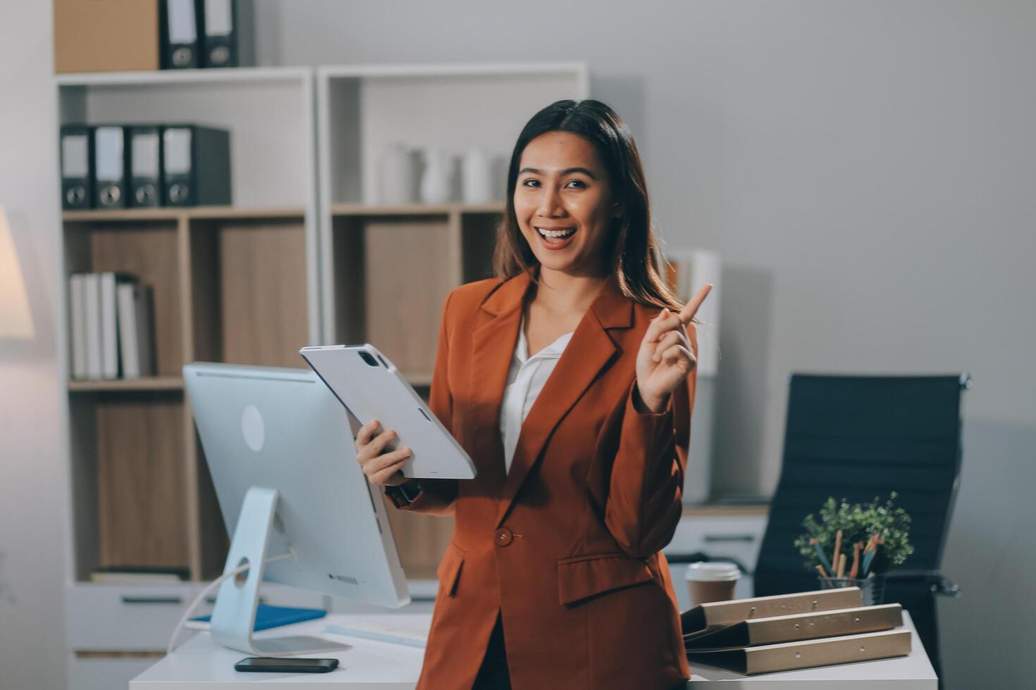 Attractive smiling Asian businesswoman standing holding tablet working and recording work details in office. photo