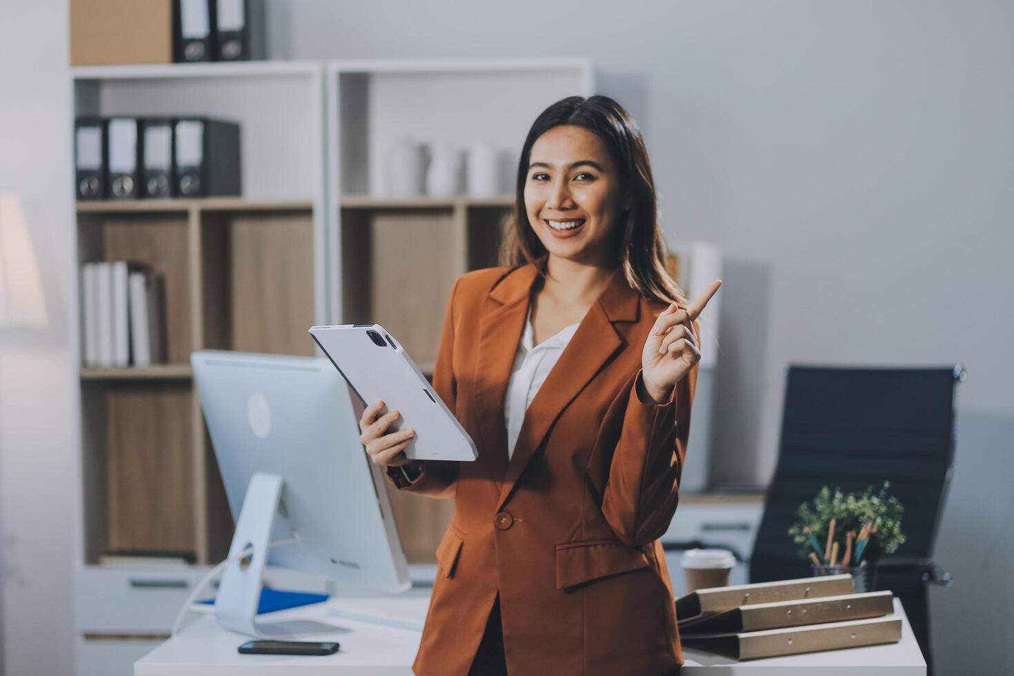 Attractive smiling Asian businesswoman standing holding tablet working and recording work details in office. photo