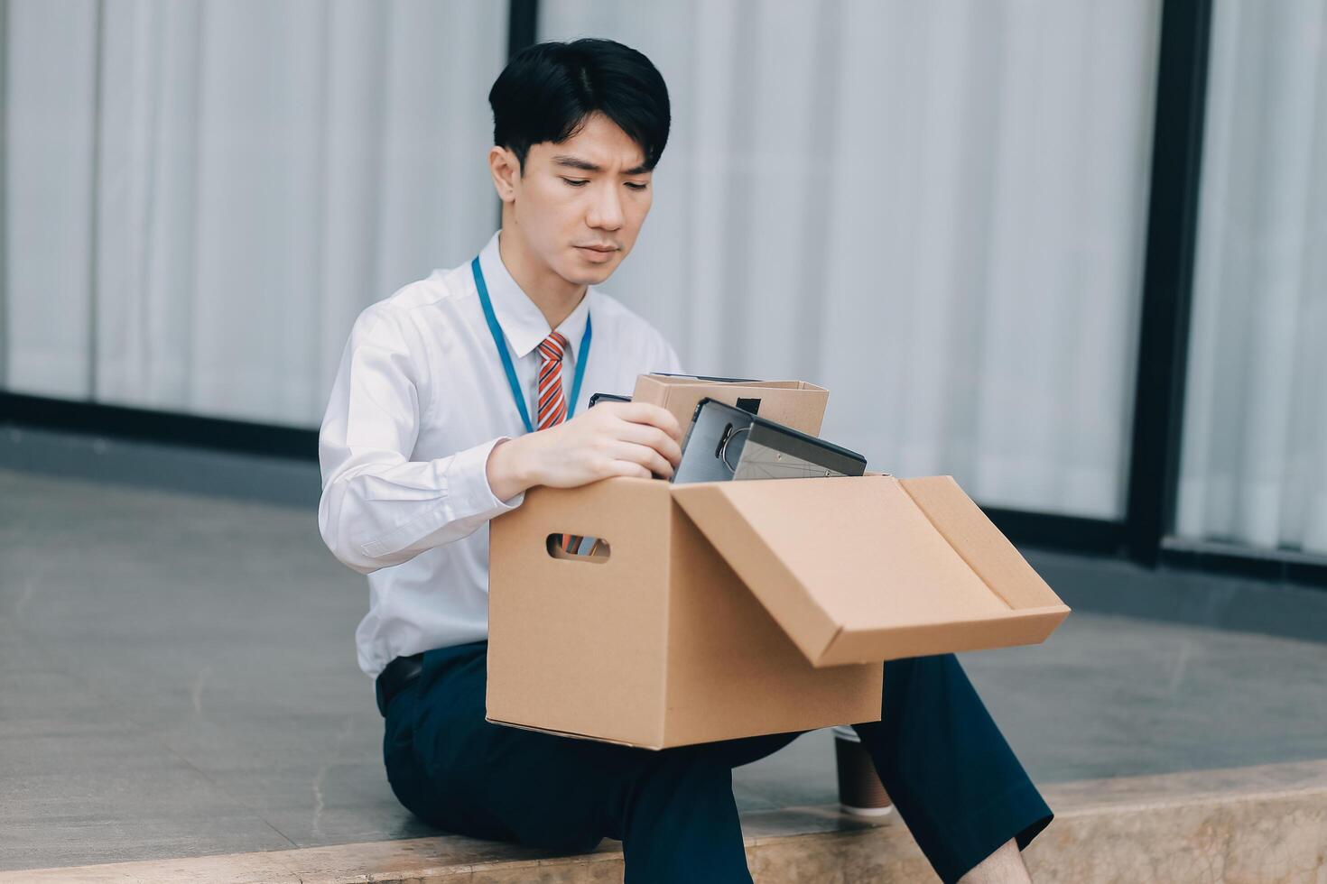 Sadness depressed Businessman with box cardboard packing personal items after losing jobs. Failure businessman sitting at stair front of building. Your fired Unemployed Jobless People Crisis photo