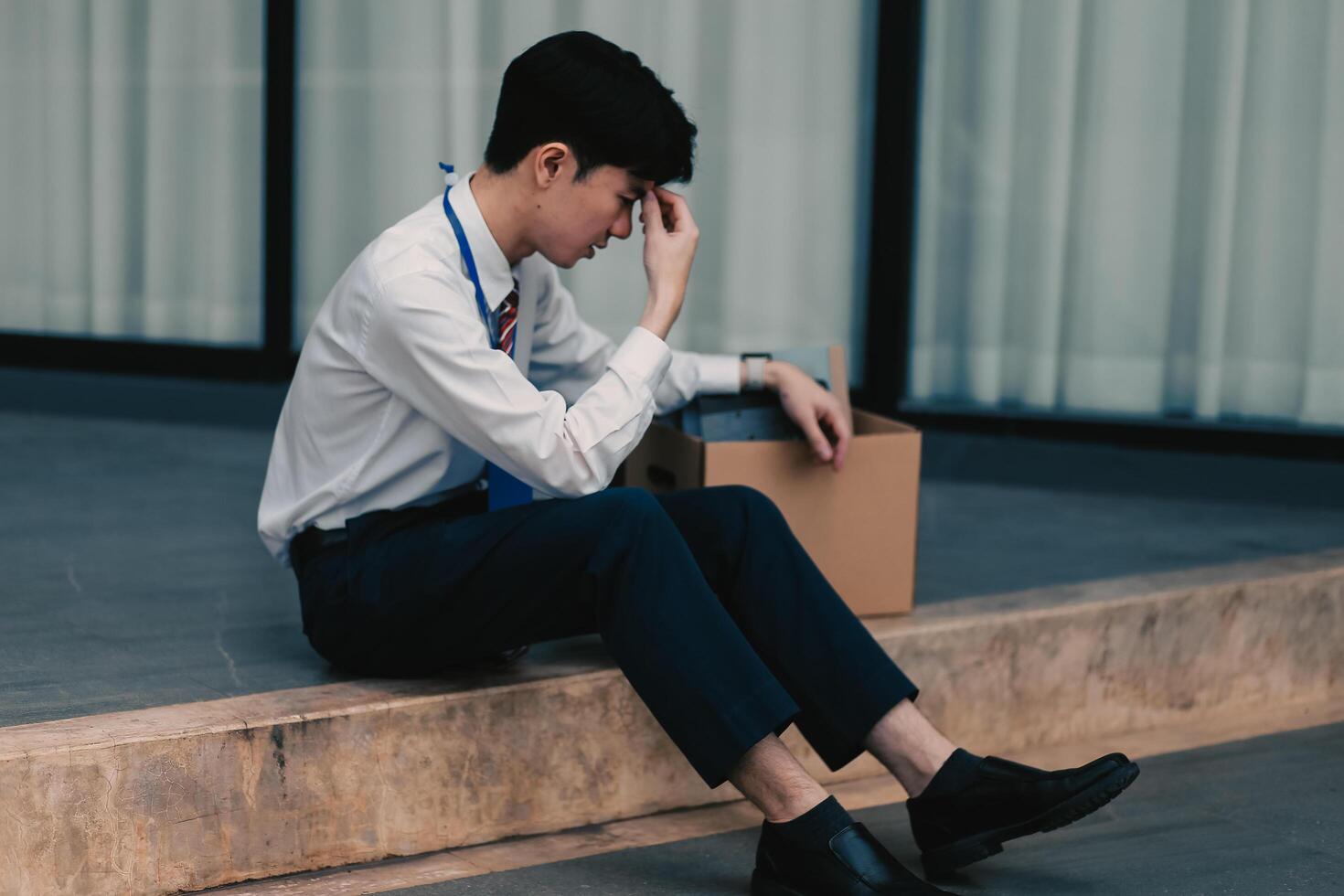 Sadness depressed Businessman with box cardboard packing personal items after losing jobs. Failure businessman sitting at stair front of building. Your fired Unemployed Jobless People Crisis photo