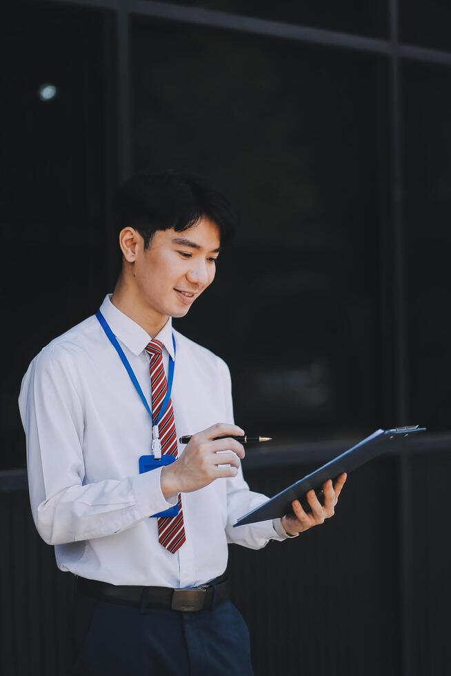 Serious businessman looking at paper documents in front of office building. Focused male manager checking reports before work while standing outdoors. photo