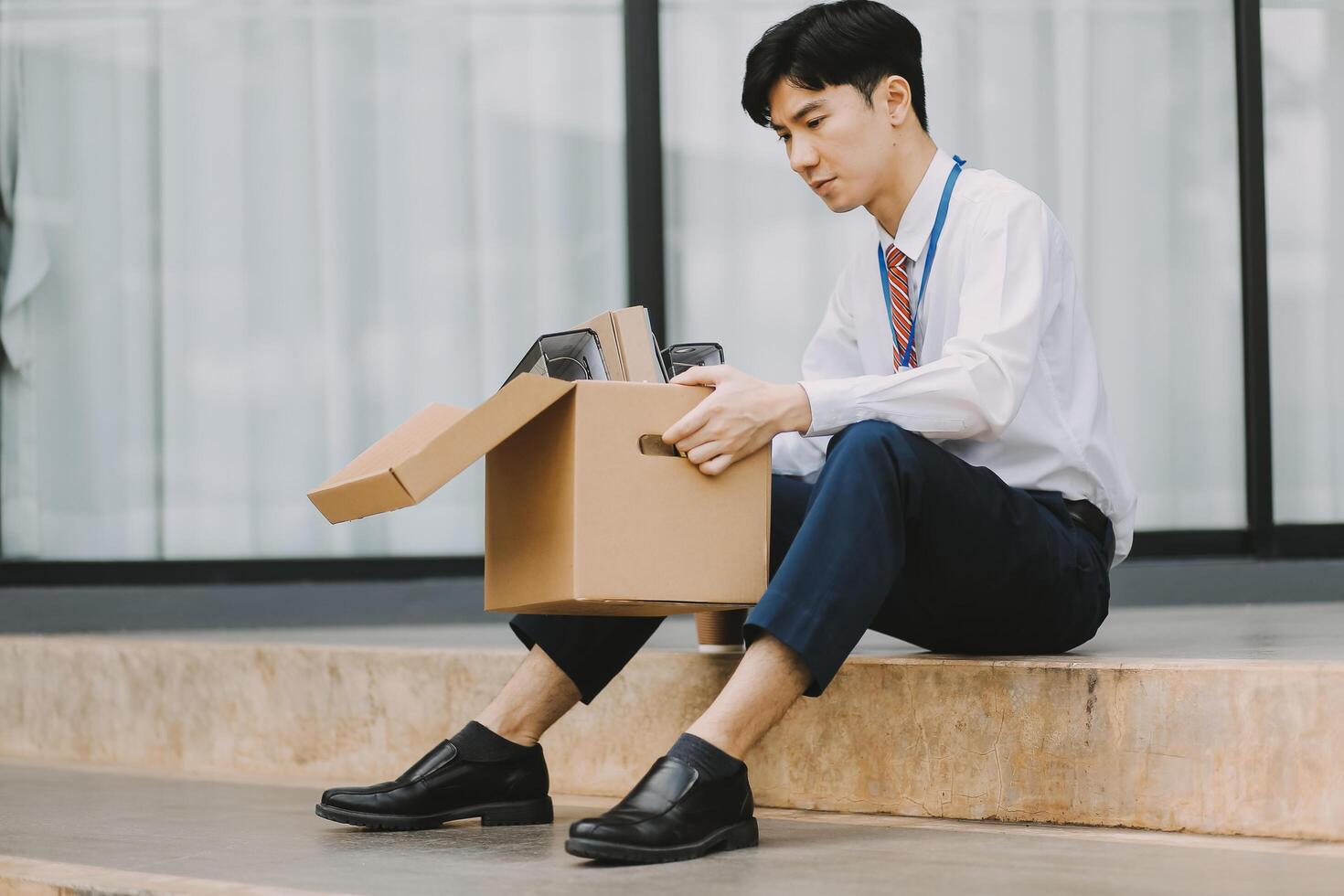 Sadness depressed Businessman with box cardboard packing personal items after losing jobs. Failure businessman sitting at stair front of building. Your fired Unemployed Jobless People Crisis photo