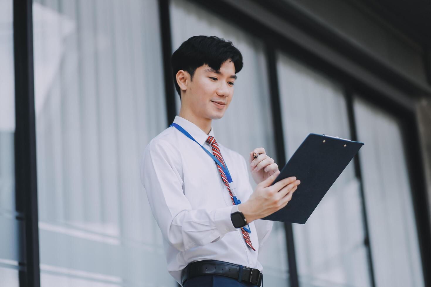 Serious businessman looking at paper documents in front of office building. Focused male manager checking reports before work while standing outdoors. photo