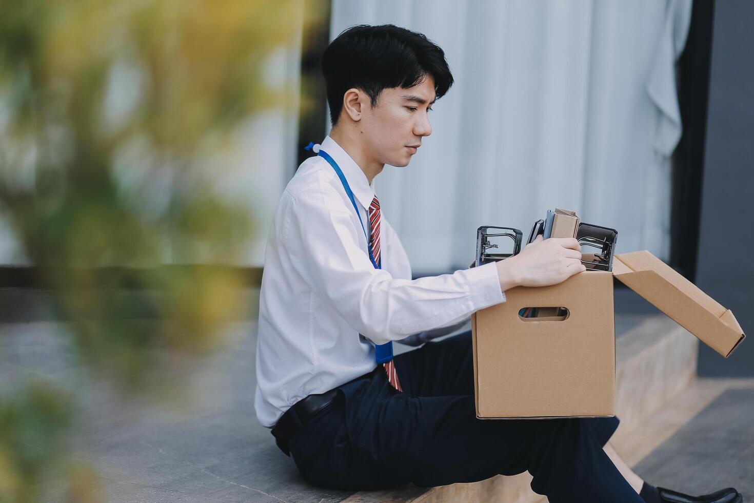 Sadness depressed Businessman with box cardboard packing personal items after losing jobs. Failure businessman sitting at stair front of building. Your fired Unemployed Jobless People Crisis photo