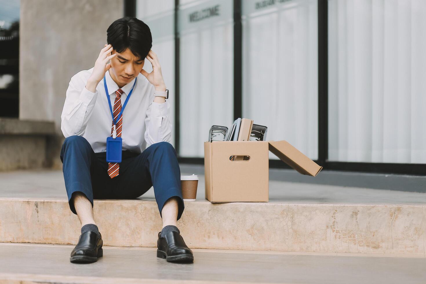 Sadness depressed Businessman with box cardboard packing personal items after losing jobs. Failure businessman sitting at stair front of building. Your fired Unemployed Jobless People Crisis photo