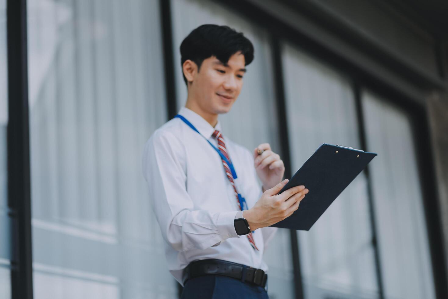 Serious businessman looking at paper documents in front of office building. Focused male manager checking reports before work while standing outdoors. photo