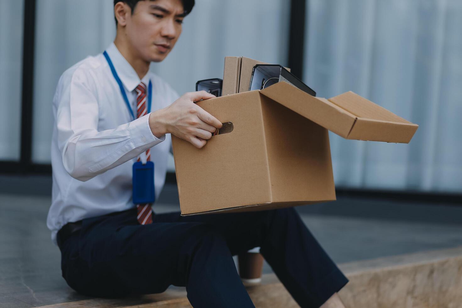 Sadness depressed Businessman with box cardboard packing personal items after losing jobs. Failure businessman sitting at stair front of building. Your fired Unemployed Jobless People Crisis photo
