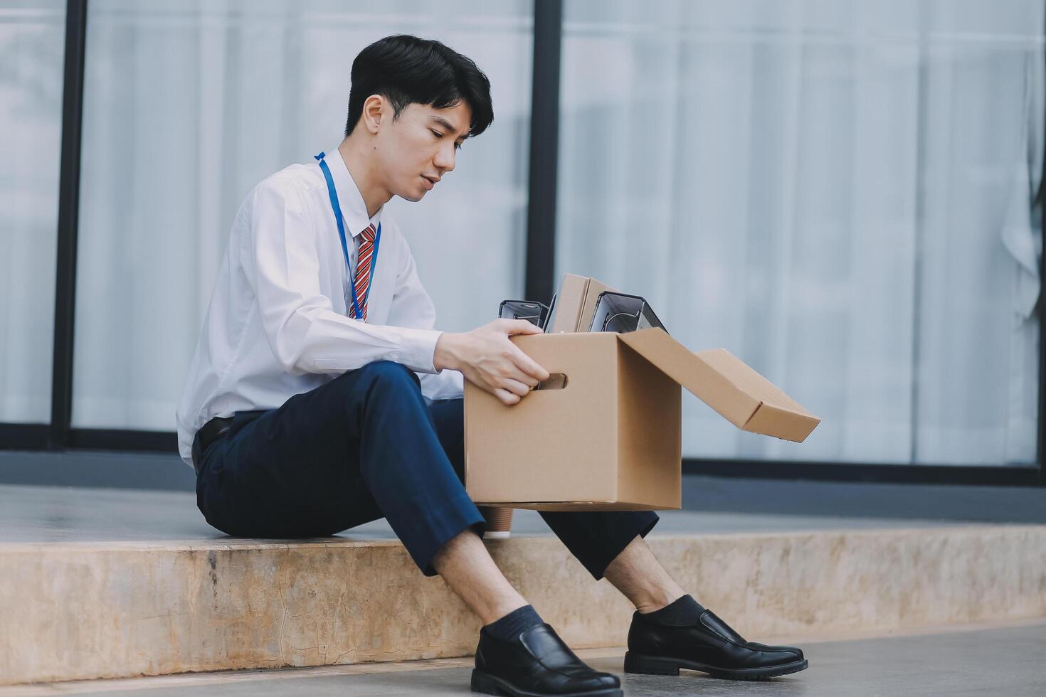 Sadness depressed Businessman with box cardboard packing personal items after losing jobs. Failure businessman sitting at stair front of building. Your fired Unemployed Jobless People Crisis photo