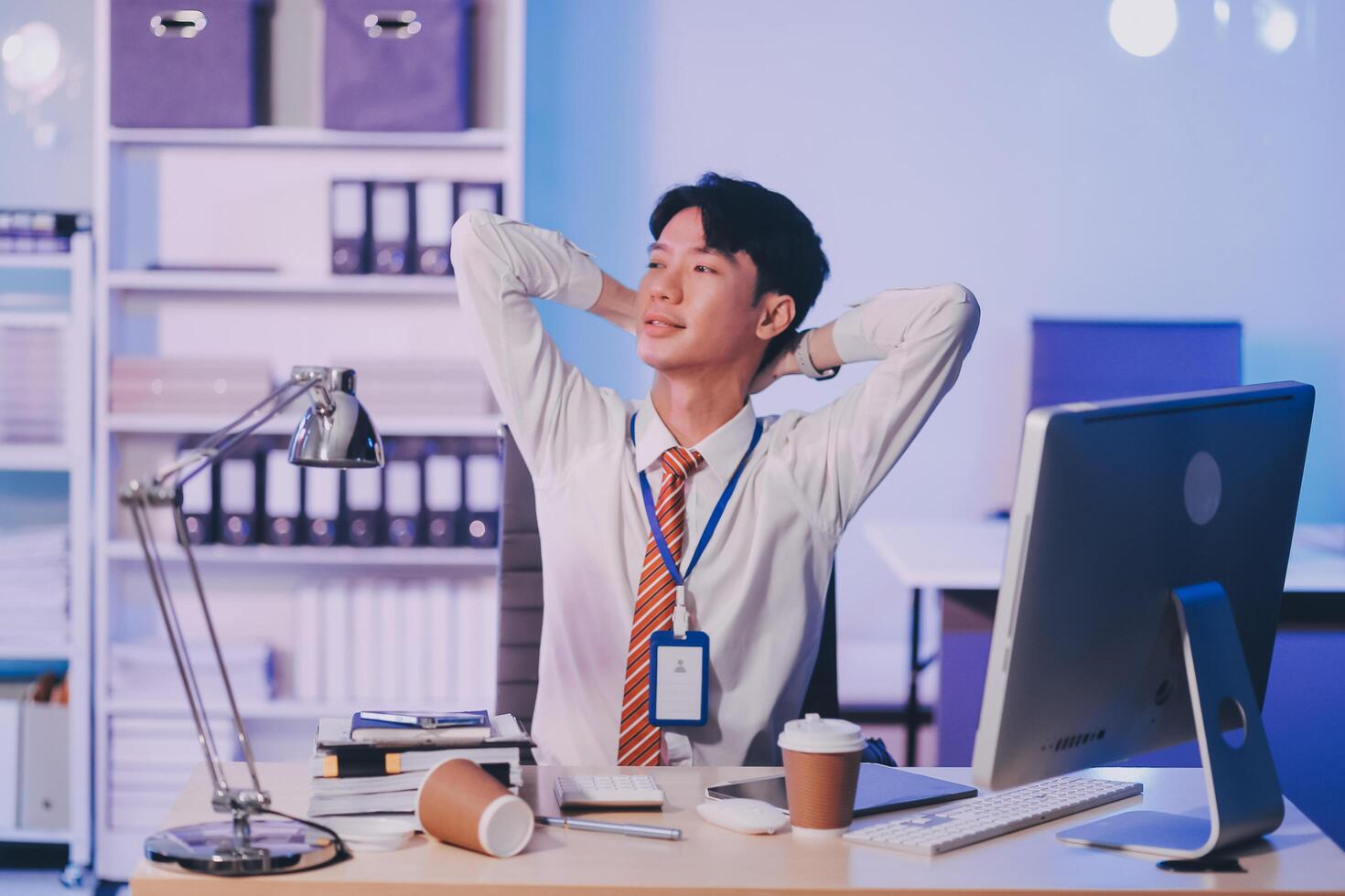 Young pensive asian man working late concentrated and serious in front of computer at night in dark office, Late night working or studying concept. photo