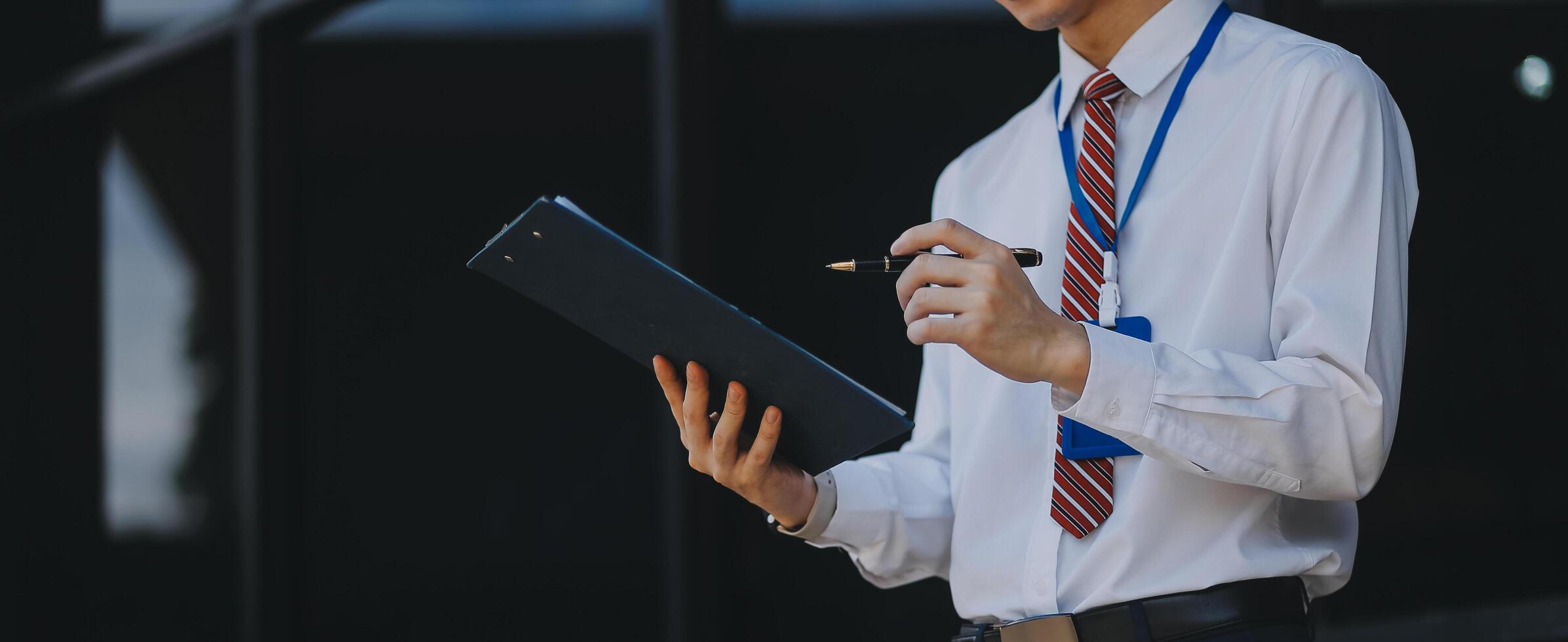 Serious businessman looking at paper documents in front of office building. Focused male manager checking reports before work while standing outdoors. photo