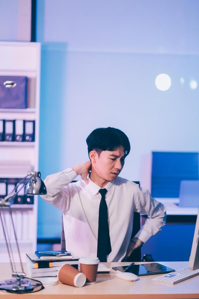 Young pensive asian man working late concentrated and serious in front of computer at night in dark office, Late night working or studying concept. photo