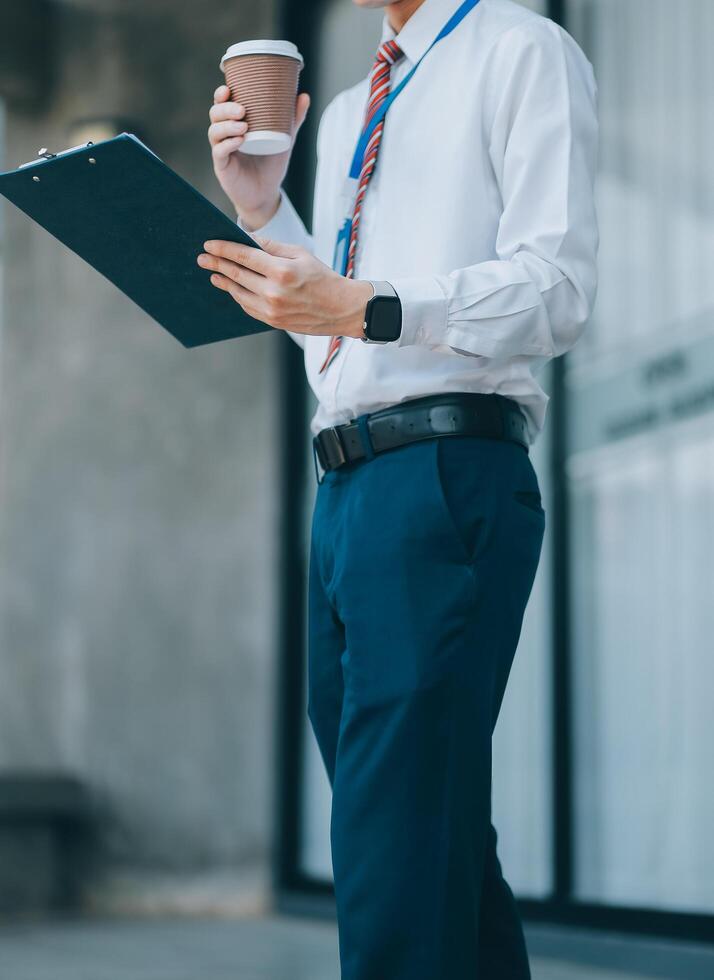 Happy businessman drinking coffee and using mobile phone in front of his office building. photo