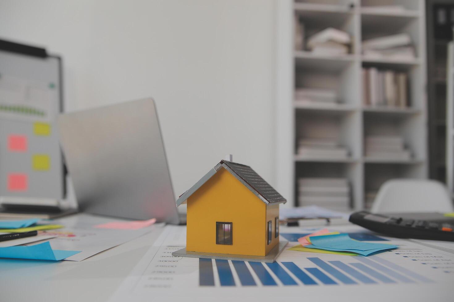 Wooden table with laptop, house keys Clipboard with pen, house model and green tree calculator, real estate concept. close up pictures photo