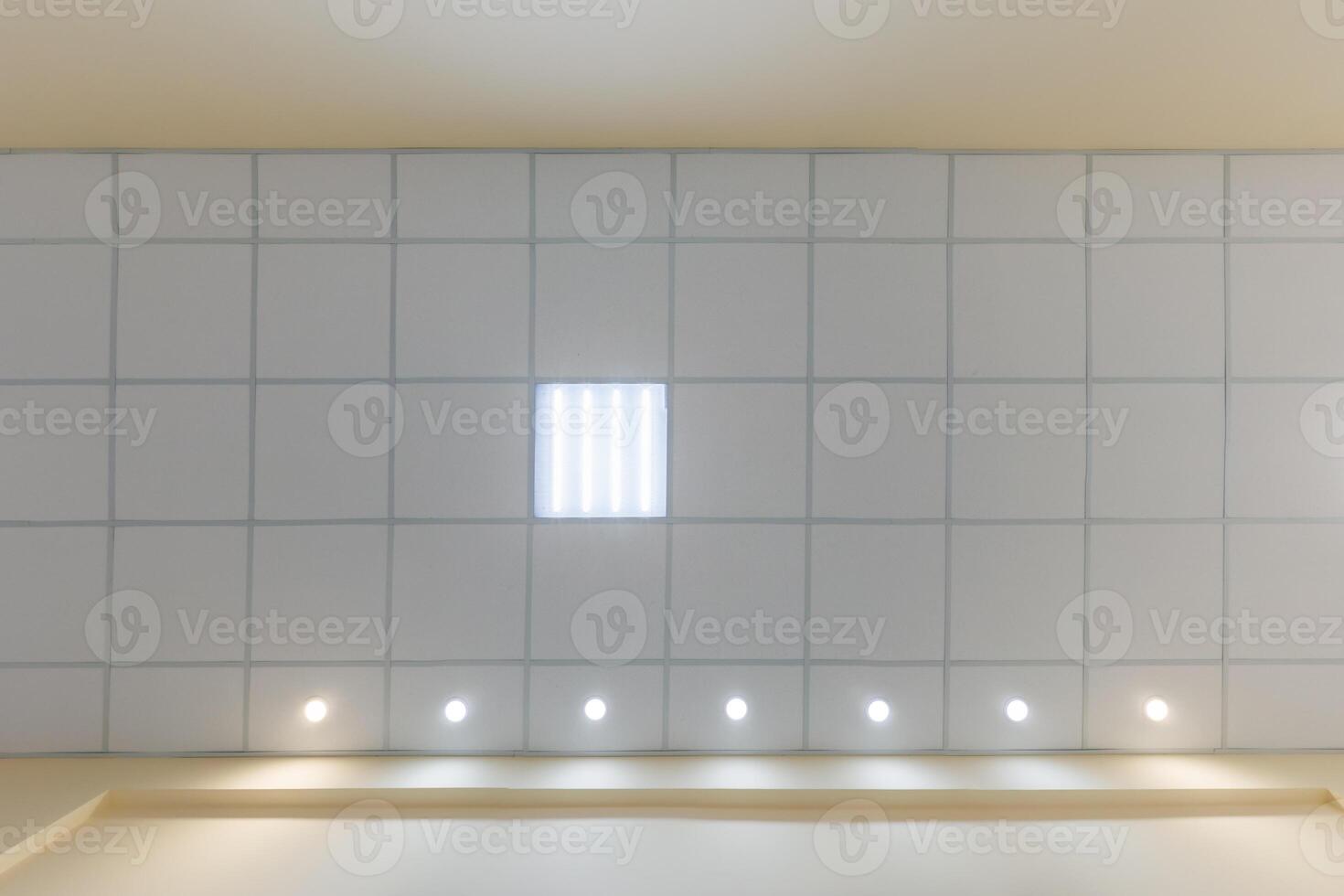 cassette stretched or suspended ceiling with square halogen spots lamps and drywall construction in empty room in house or office. Looking up view photo