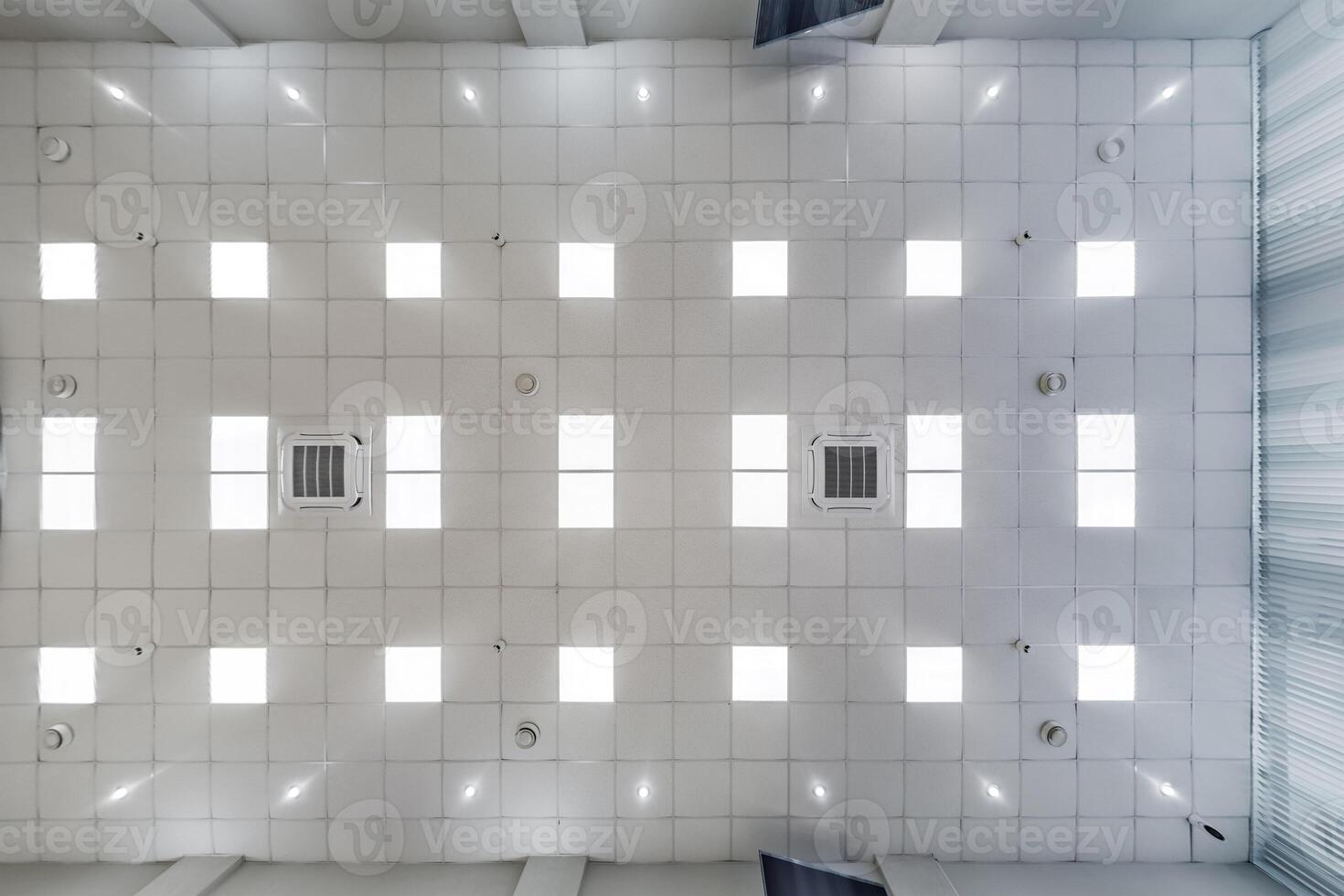 cassette stretched or suspended ceiling with square halogen spots lamps and drywall construction in empty room in house or office. Looking up view photo