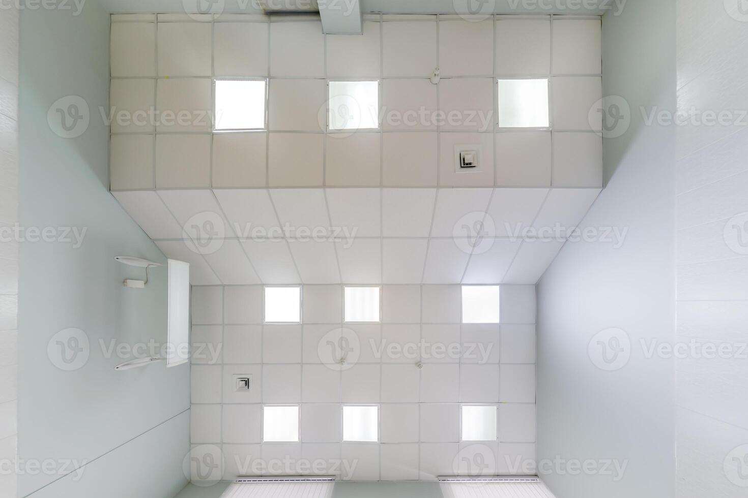 cassette stretched or suspended ceiling with square halogen spots lamps and drywall construction in empty room in house or office. Looking up view photo
