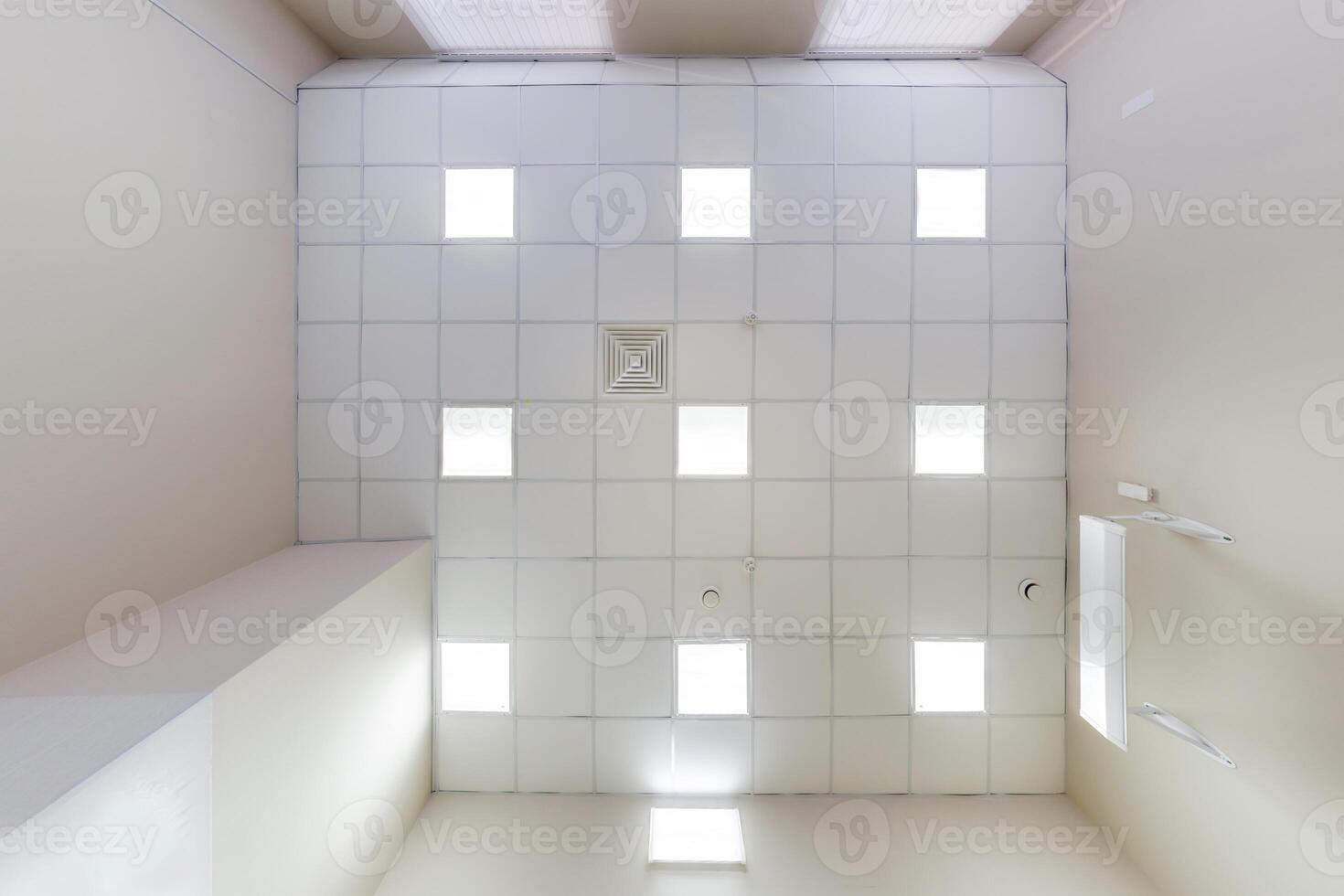 cassette stretched or suspended ceiling with square halogen spots lamps and drywall construction in empty room in house or office. Looking up view photo