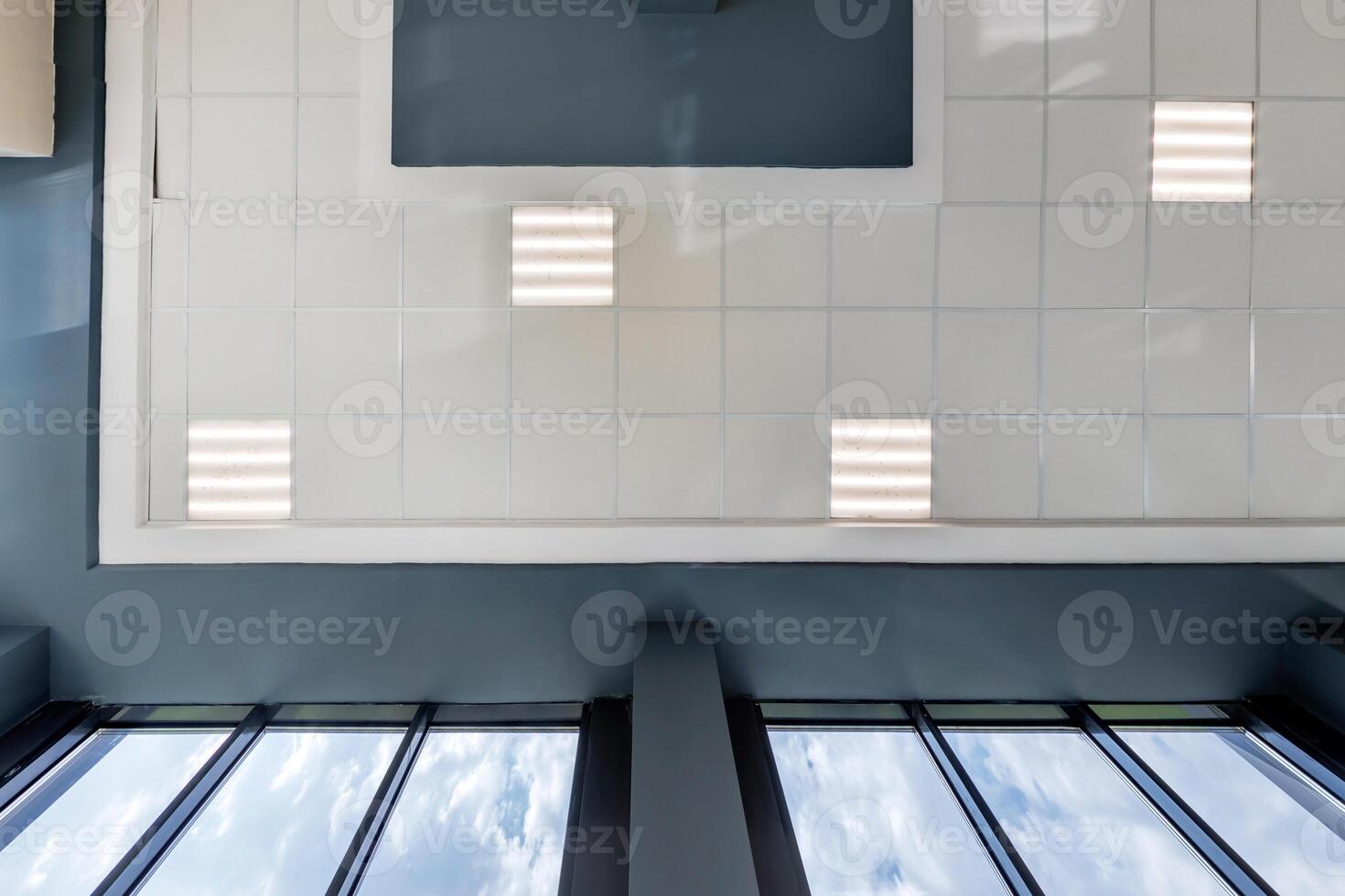 cassette stretched or suspended ceiling with square halogen spots lamps and drywall construction in empty room in house or office. Looking up view photo