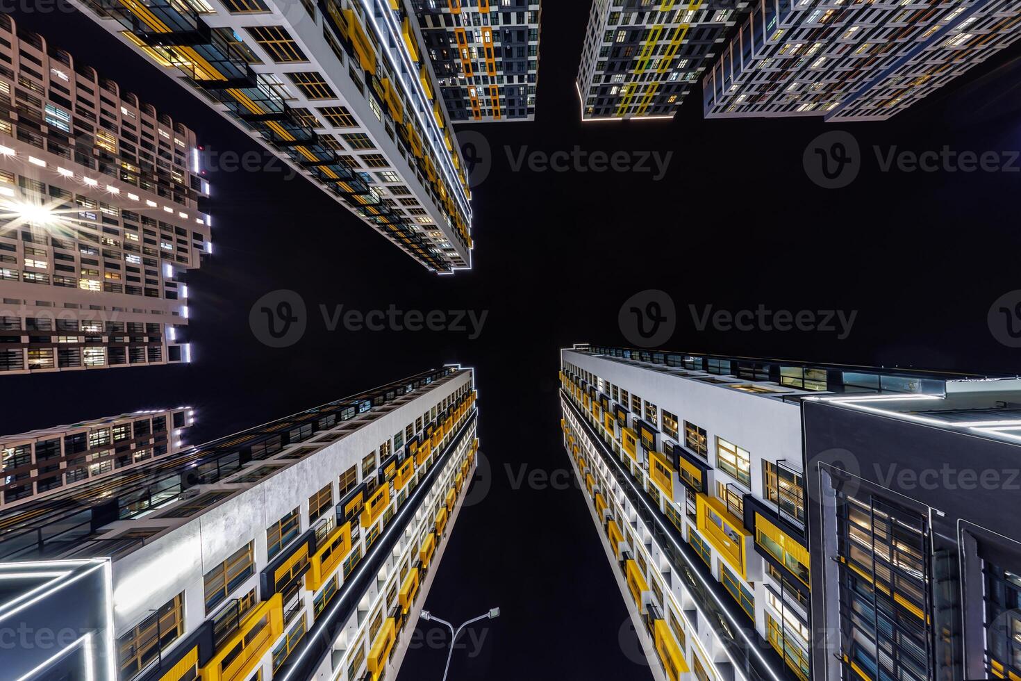Low-angle view of colorful, illuminated high-rise buildings surrounding a dark night sky, showcasing modern architecture and urban living. photo