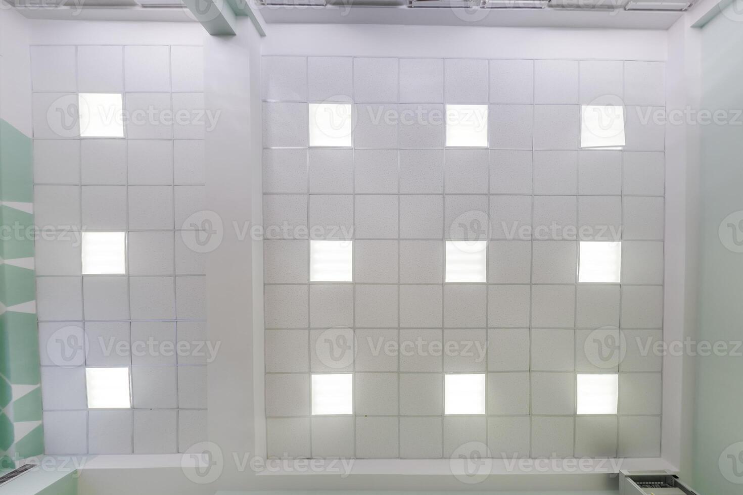 cassette stretched or suspended ceiling with square halogen spots lamps and drywall construction in empty room in house or office. Looking up view photo