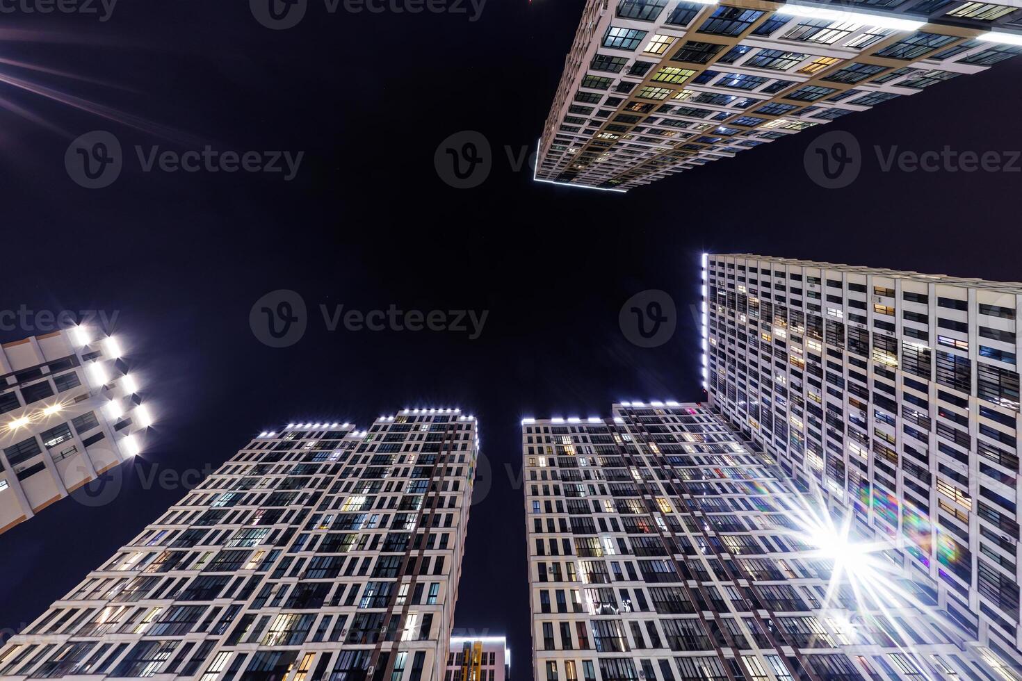 Low-angle view of colorful, illuminated high-rise buildings surrounding a dark night sky, showcasing modern architecture and urban living. photo