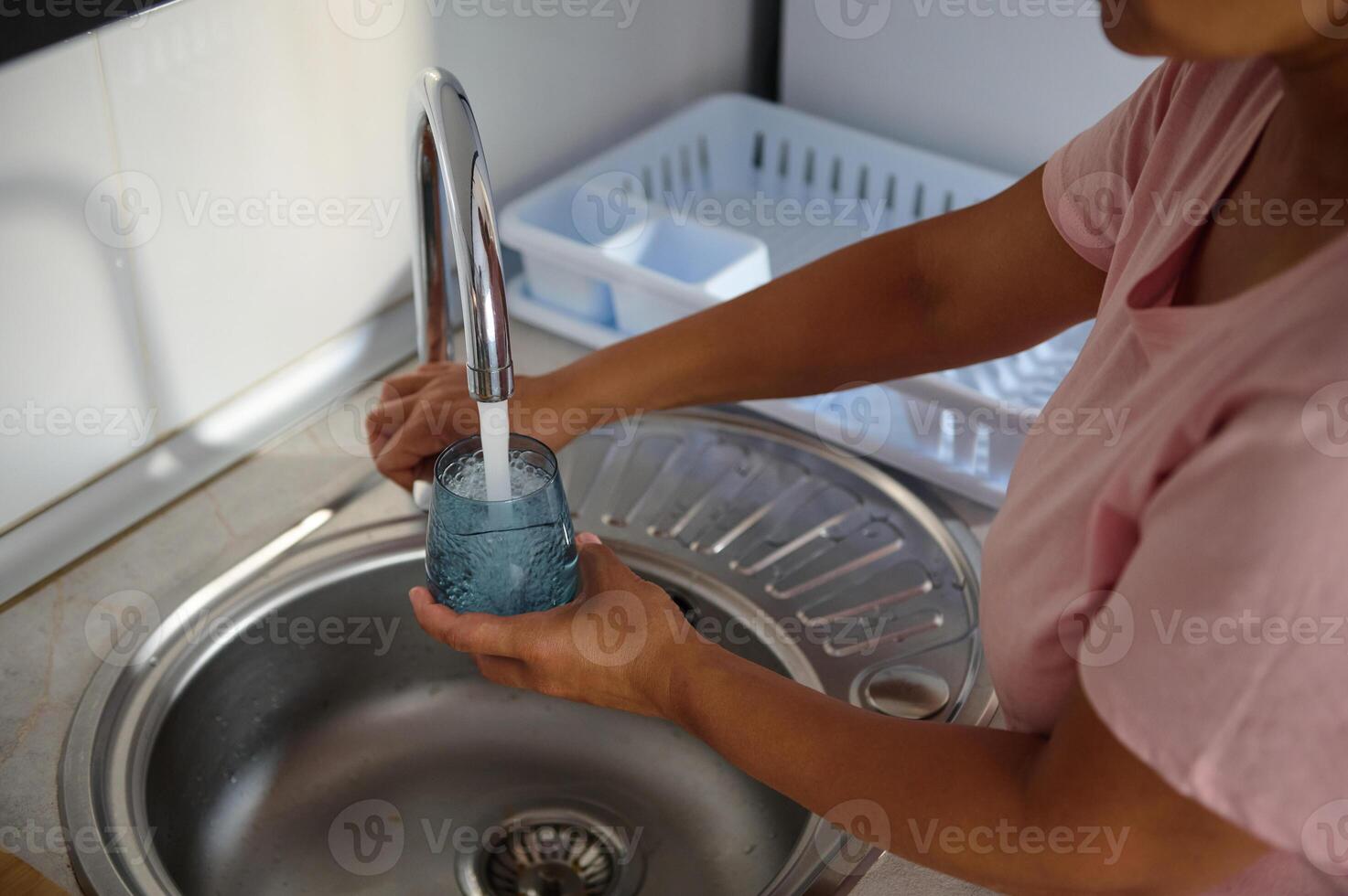 Person filling a glass with fresh water from a kitchen faucet, emphasizing hydration and sustainability in a modern home environment. photo