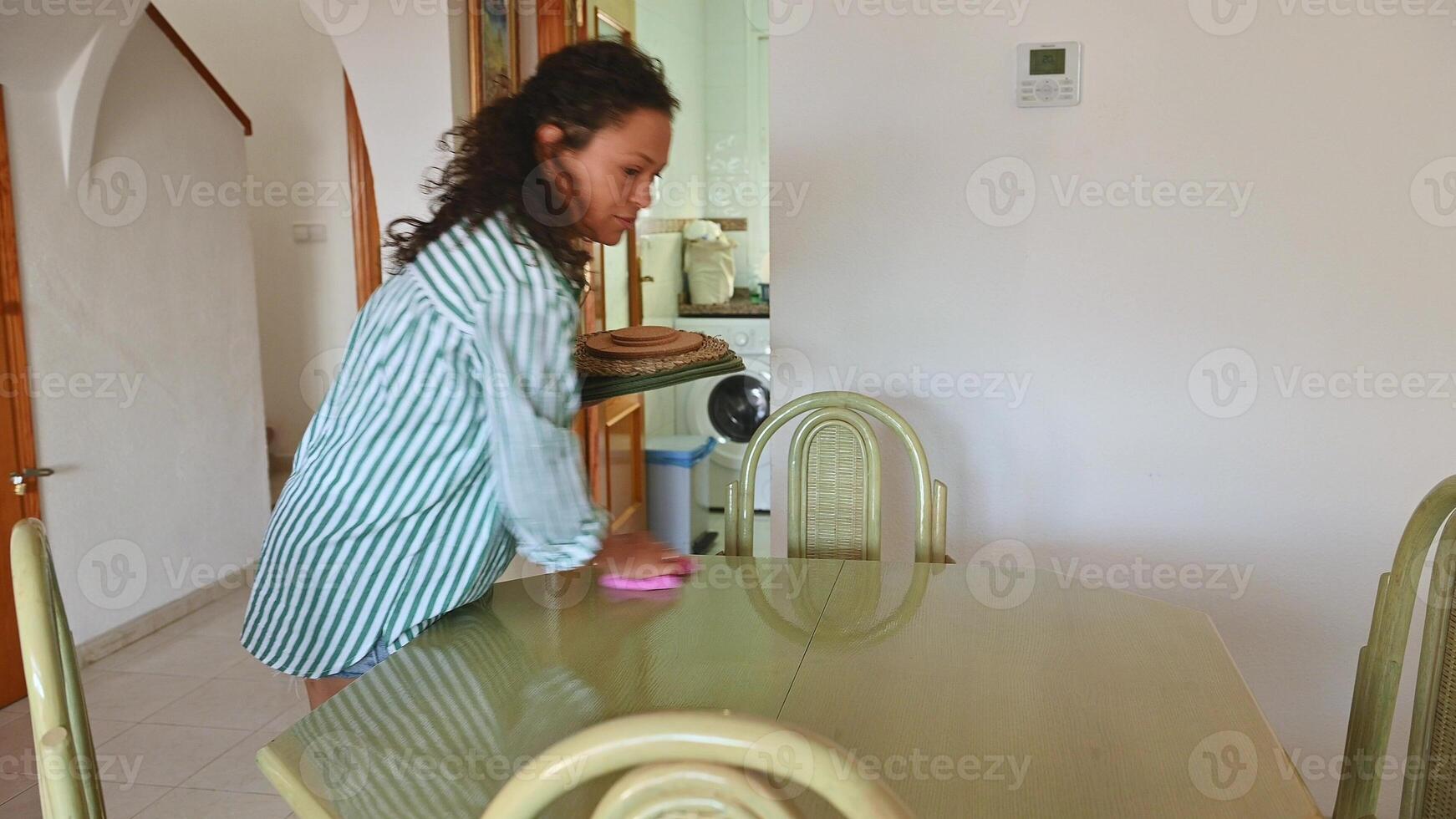 Woman cleaning dining table at home, maintaining a clean and organized living space for daily routines. photo
