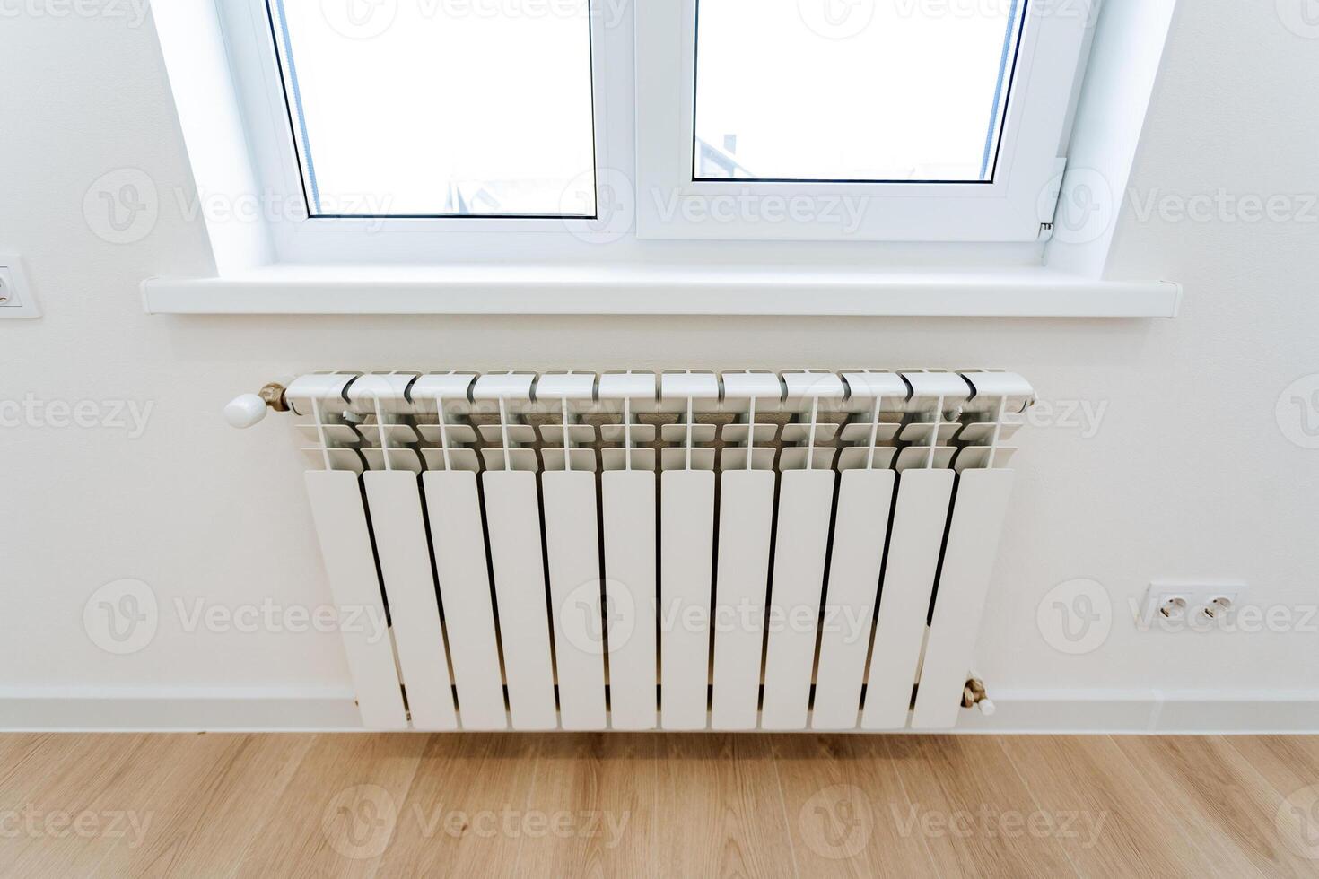 The heating radiator hangs in the room under the window, the heating system in the house, the heating of cold air from the window. photo