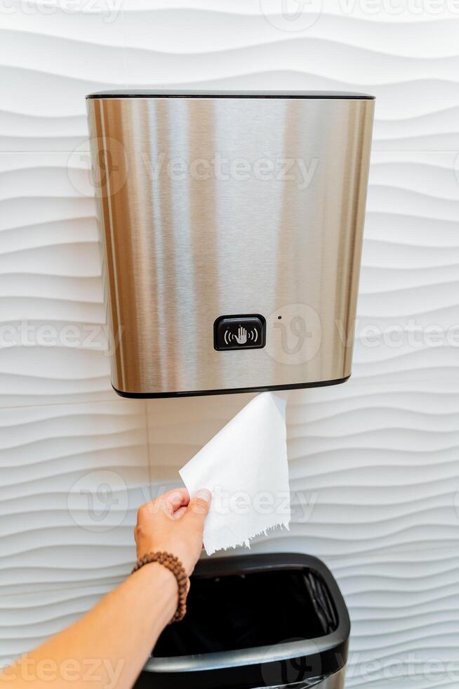 Paper towels, hand tears off a piece of paper, wipe hands in the toilet, paper dispenser, touch control, hand sensor, wrist bracelet. photo