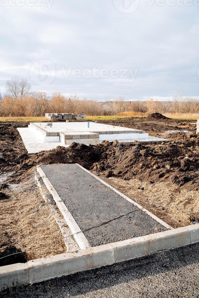 Stages of construction of a country house, construction site, asphalt path to the future house, concrete base cushion for a new country house. photo