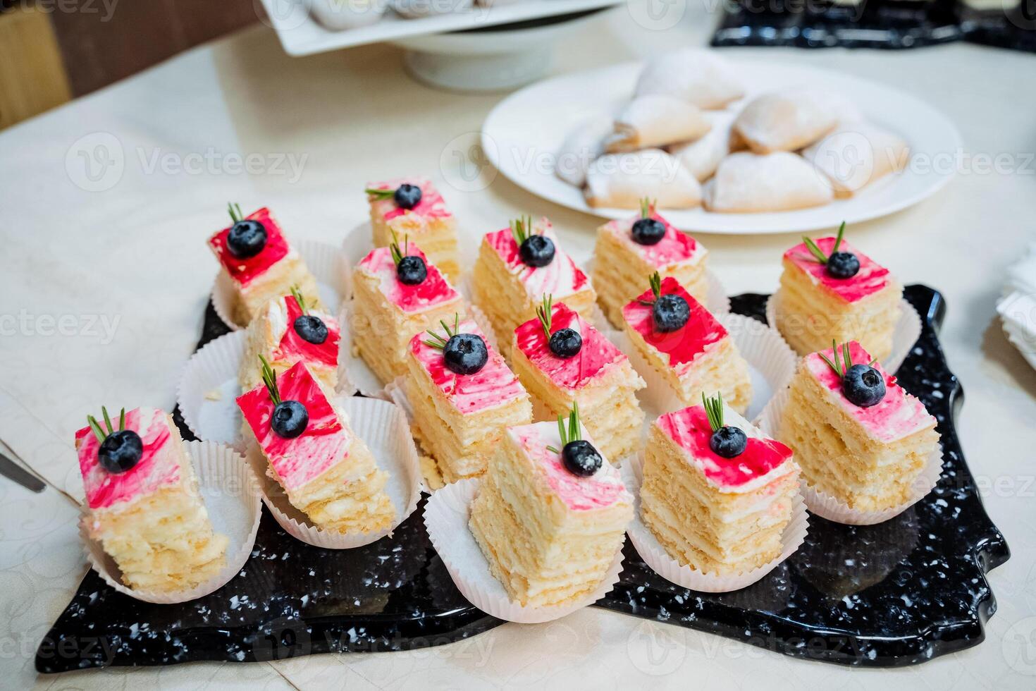 Honey cake on a plate cut into pieces, small pieces of cake with blueberries on top, serving sweets on a marble board, buffet table. photo