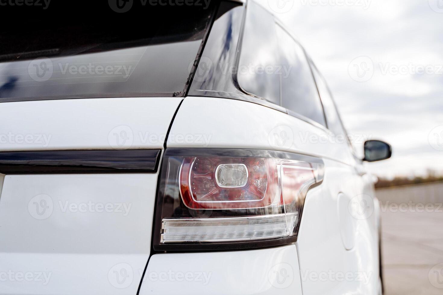 Glass headlight at the rear of the car, parking lights, red brake light, part of the car rear view, white body color. photo