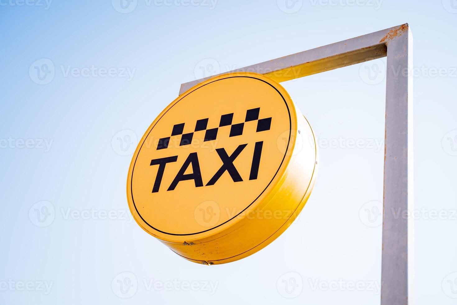 A taxi sign hangs against the sky, a taxi stop, a yellow banner with black text, letters in a circle, taxi checkers, sunlight. photo