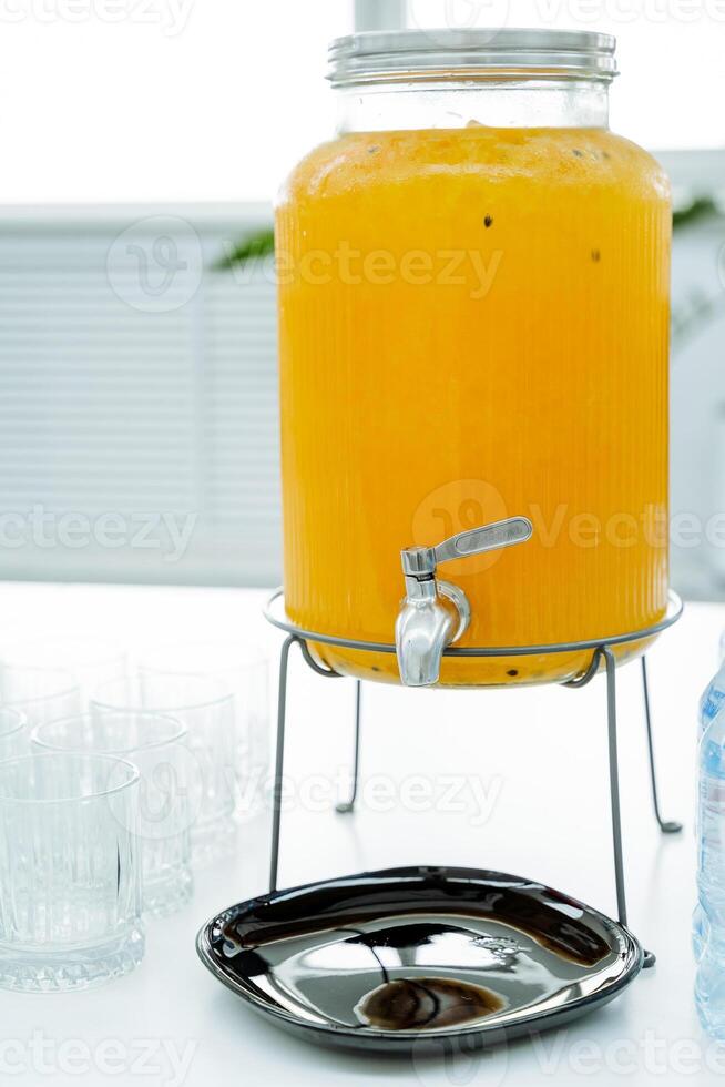 Orange juice in a jar with tap, festive table setting, orange drink, jug with sweet drink. photo
